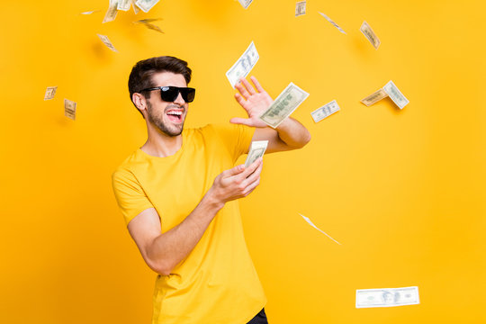 Photo of young handsome careless guy throwing money banknotes away wealthy person wear sun specs casual t-shirt isolated bright yellow color background