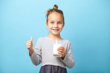 Cheerful child girl drinks milk and shows thumbs up.