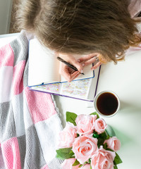 Woman doing devotional Bible study and writing in a journal. Pink roses and coffe on a white table. 