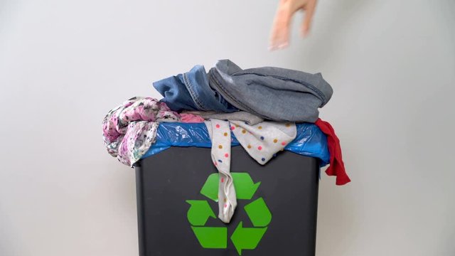 Distribution of waste for recycling at home. A woman's hand puts old clothes in a bin with a sign of recycling