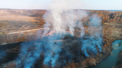 Forest and field fire. Dry grass burns, natural disaster. Aerial view. A large burned field, burning occurs on the banks of a small river.