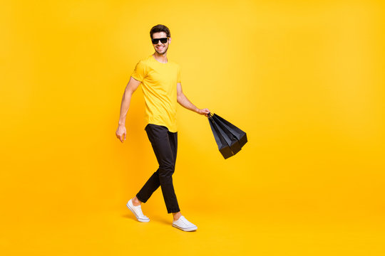 Full body photo of handsome guy carry boutique bags make abroad shopping go fashionable mall wear casual t-shirt black pants isolated yellow color background