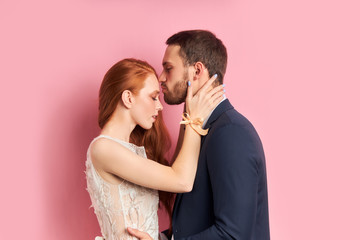Kissing forehead of redhaired woman, bearded man in tuxedo. Woman in white wedding dress hug her...
