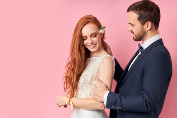 Bearded fiance in love with redhaired woman, long hair. Isolated pink background