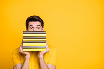 Close-up portrait of his he nice attractive funny brunette guy holding in hands hiding behind pile of book scary difficult knowledge isolated over bright vivid shine vibrant yellow color background