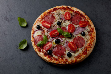Pizza with salami, mozzarella cheese, cherry tomatoes, black olives, red onion and oregano. Home made food. Concept for a tasty and hearty meal. Black stone background. Copy space