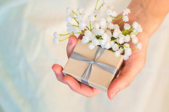 Female Hand Holds A Small Gift Box And White Flowers