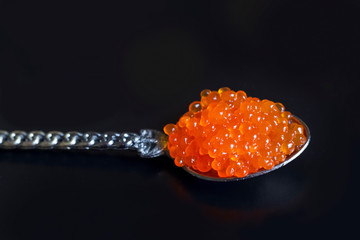 Red caviar on a small spoon, black background.