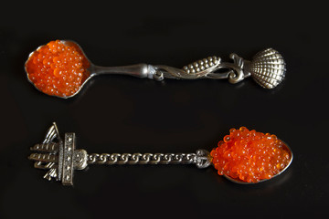 Red caviar on spoons, black background.
