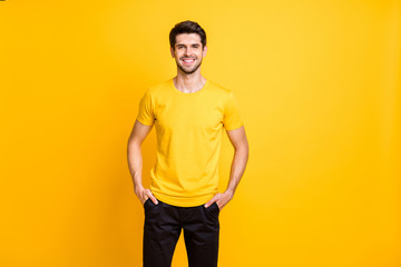Photo of cheerful attractive man holding hands in pockets of his black pants smiling toothily with...