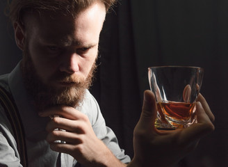 Portrait of a pensive handsome young man, with a glass of alcohol in his hands.