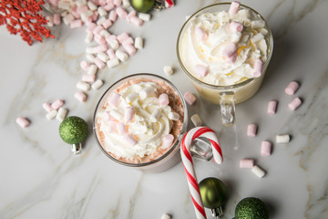 Heiße, dunkle Trinkschokolade zu Weihnachten mit Sahne, Marshmellows, Christbaumkugeln grün, Zuckerstangen, Glitzer Schneeflocken rot auf Marmor hell Hintergrund 