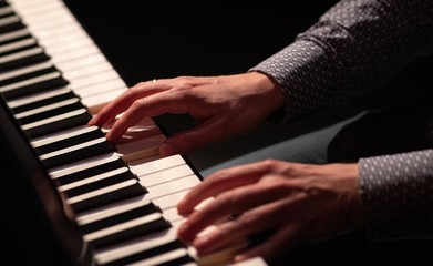 Hands playing piano in a dark theatre blouse white and black keys