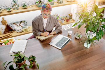 Modern caucasian woman 50-60 years old sit working with laptop, notebooks, papers, plants on table. Light business office