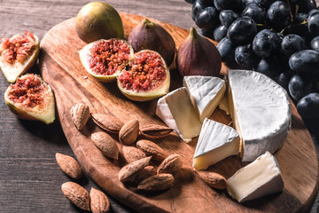 Cheese plate served with grapes, figs and nuts on a wooden background.