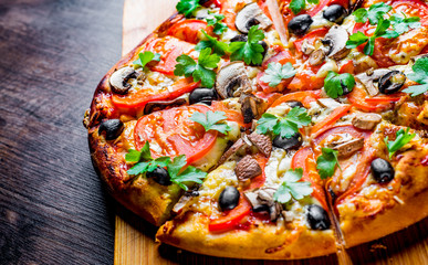 sliced Pizza with Mozzarella cheese, Tomatoes, pepper, olive, mushrooms, Spices and Fresh leaf. Italian pizza on wooden table background