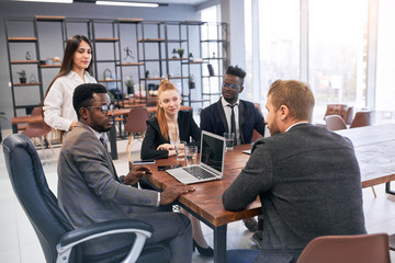Young business people gathered in meeting office, everyone dressed in formal suits, using laptop. Business concept