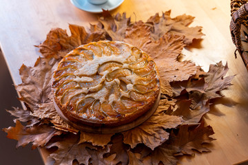 Freshly baked homemade apple pie with cup of tea near basket with apples on wooden table and autumn...