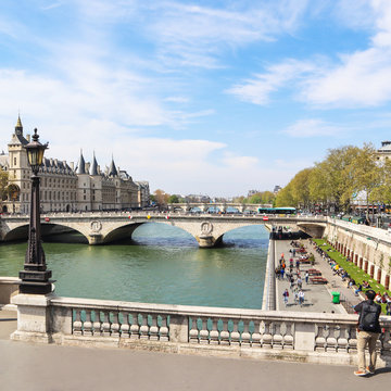 Cityscape of Paris and Saint-Michel bridge across Seine river. A tourist photographs a beautiful view of the promenade with people resting on sunny day in spring