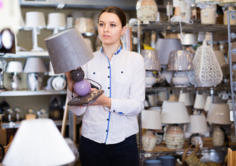 Girl is choosing modern table lamp in furniture store.