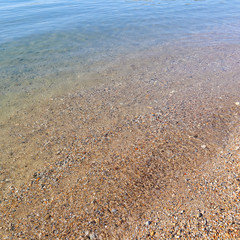 Beautiful background of blue calm sea with little fish, sand and pebbles. Rest and relaxation on the sea coast