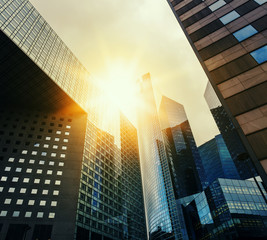 Skyscraper glass facades on a bright sunny day with sunbeams in the blue sky. Modern buildings in business district. Economy, finances, business activity concept. Bottom up view	