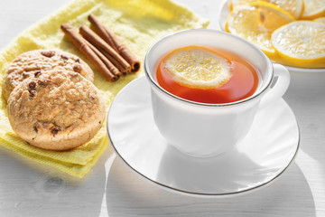 White cup of tea with lemon, cookies and cinnamon.