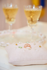 Two glasses of a champagne and pillow with wedding rings..