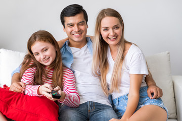 Happy family on couch in living room, including father and mother and daughter, enjoy watching television together, with remote control