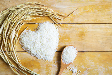 White rice in heart shape and wooden spoon with rice husk on wood background.Healthy food concept