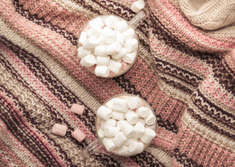 Hot winter drink with cocoa, chocolate and marshmallows in cups on gray background with knitted warm sweater, top view
