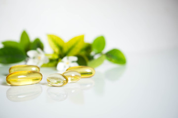 Close up soft capsules with leaves and white flora on white background with copy space for text.