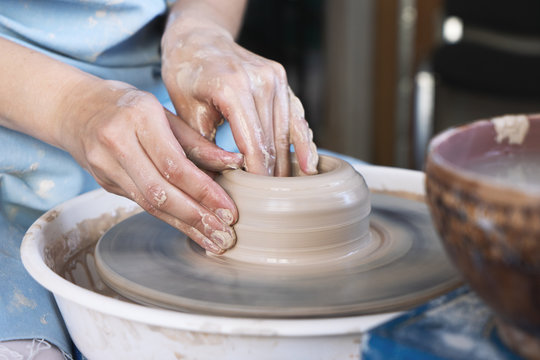 Girl Potter sculpts a pitcher of clay on a Potter's wheel.