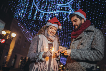 Young loving couple burning sparklers by holiday illumination on new years eve.