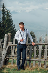 Fototapeta premium Pretty groom in rustic style stand on a background of mountains .