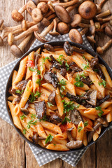 Italian penne pasta with Armillaria mellea mushrooms, tomatoes, cheese and parsley close-up in a plate. Vertical top view