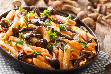 Serving penne pasta with roasted honey mushrooms and tomato sauce close-up in a plate. horizontal
