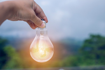 hand holding light bulb against nature, icons energy sources for renewable, 