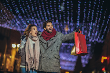 Couple with gift bag on Christmas lights background during walking in the city at evening