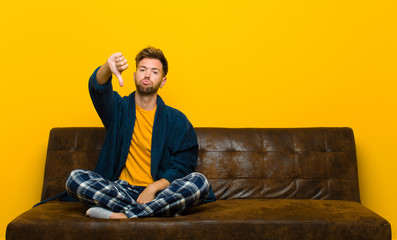 young man wearing pajamas feeling cross, angry, annoyed, disappointed or displeased, showing thumbs...