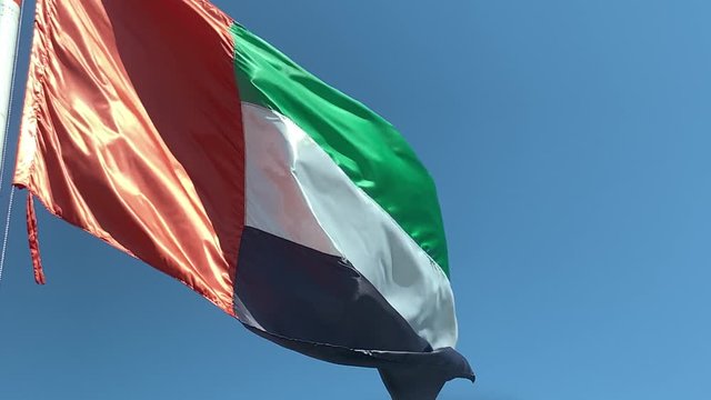 SLOW MOTION Flag of United Arab Emirates against blue sky in a summer day UAE flag waving in Dubai city , national symbol of UAE., uae flag perfect for film, news, digital composition, uae flag day