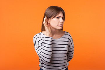 Portrait of attentive nosy young woman with brown hair in long sleeve striped shirt standing,...