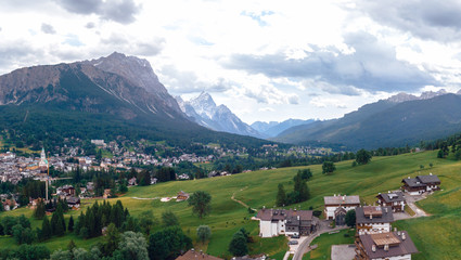 Fototapeta na wymiar Tourist town Cortina d'Ampezzo, panoramic view with alpine green landscape and massive Dolomites Alps. View of houses and hotels, the city from a height. Province of Belluno, South Tyrol, Italy.