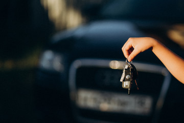 Child's hand holding car keys on black car background