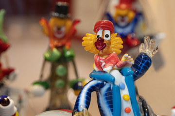Funny clown of colored glass. In the background, a blurry image of other glass figures. Selective focus.