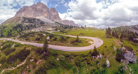 Aerial view of winding road surrounded by mountains, traveling by motorcycle or car, two cyclists riding bicycles on the road, Falzarego Pass, Dolomites, Italy. Cortina d’Ampezzo.