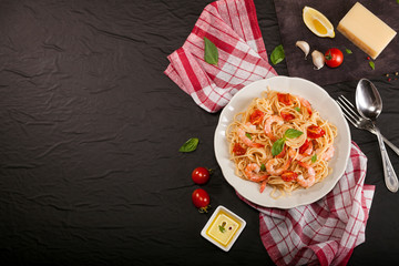 Pasta spaghetti with shrimps, dried tomato and basil on black background. Healthy meal. Italian food. Top view. Flat lay