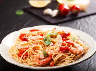 Pasta spaghetti with shrimps, dried tomato and basil on black background. Healthy meal. Italian food.