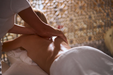 Professional masseur doing hand massage to pleasant blonde woman lying on massage couch, resting in beauty spa center, spa, health and healing concept