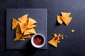 Tortilla nacho, traditional mexican snack, with salsa sauce on a black background.